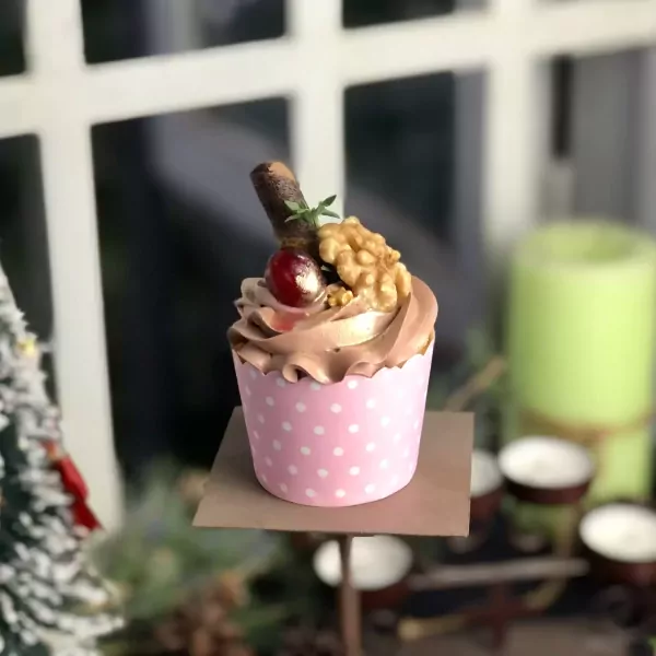 Chocolate cupcake with cherry, walnut, and chocolate stick topping in a pink polka-dot wrapper.