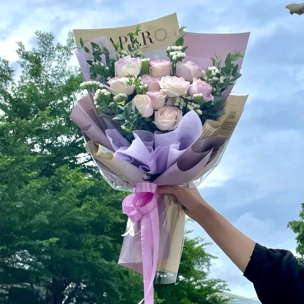 A bouquet of pale pink and white roses with eucalyptus, wrapped in purple and brown paper with a pink ribbon.