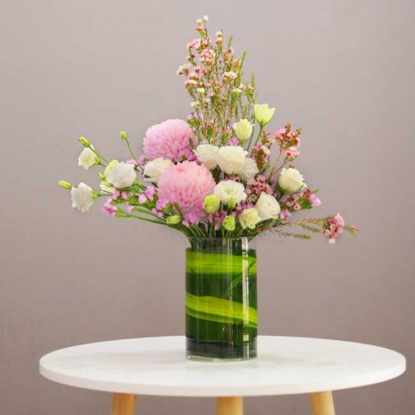 A floral arrangement of pink and white flowers in a green glass vase on a white table.