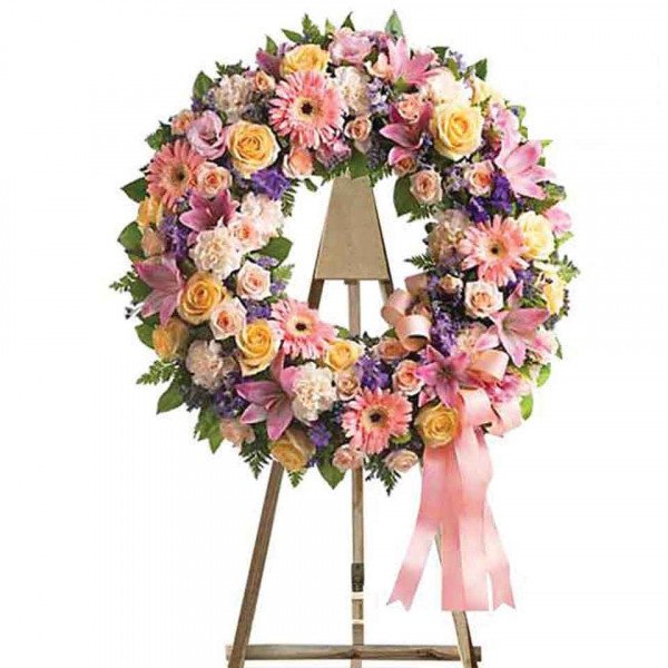 Funeral wreath with pink and yellow roses, lilies, and carnations on an easel.