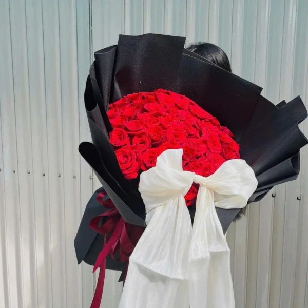 A luxurious bouquet of 50 red roses wrapped in black paper with a sheer white bow.