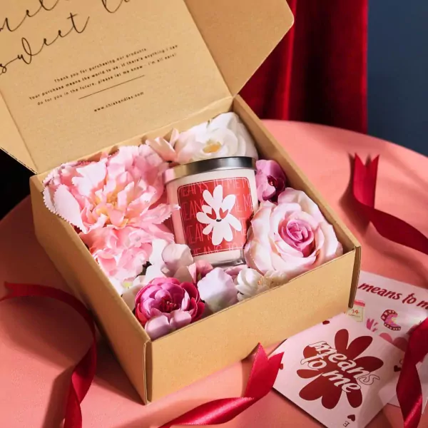 Gift box with a scented candle, pink flowers, and ribbons.