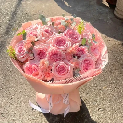 Pink roses and carnations in a pastel pink bouquet tied with white ribbon.