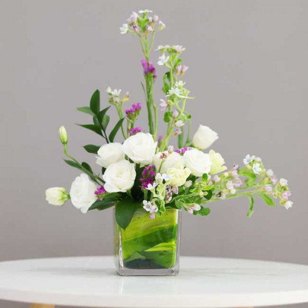 White lisianthus with purple and blue accents in a square glass vase.