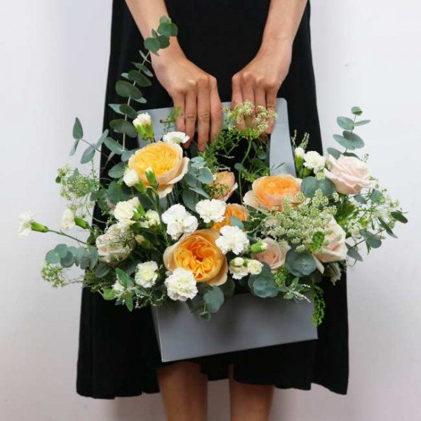 Orange and white flowers in a gray box, held by a person in a black dress.