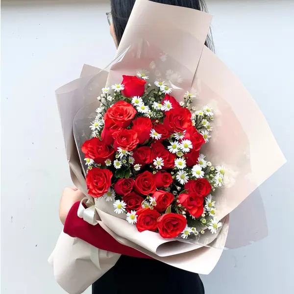 Bouquet of red roses with white filler flowers, wrapped in beige paper and tied with a cream ribbon.