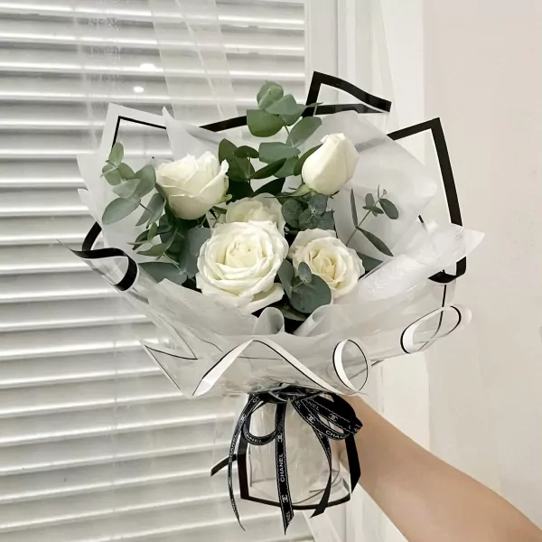 Bouquet of white roses with eucalyptus, wrapped in clear paper with black trim and ribbon.
