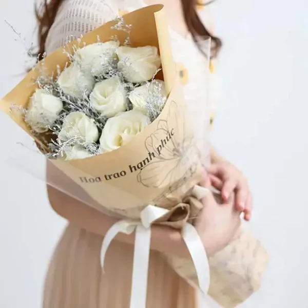 Bouquet of white roses with greenery, wrapped in brown paper and tied with a white ribbon.