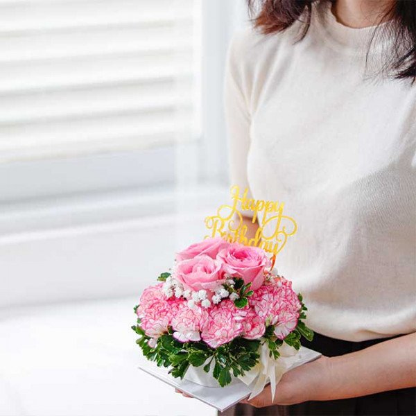 Pink roses and carnations cake with "Happy Birthday" topper, held by a person.