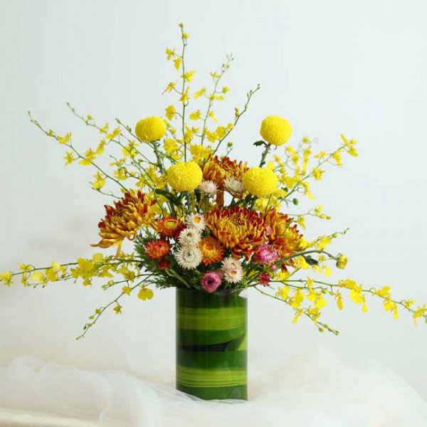 Vase of yellow and orange chrysanthemums and delicate yellow flowers with delicate greenery.