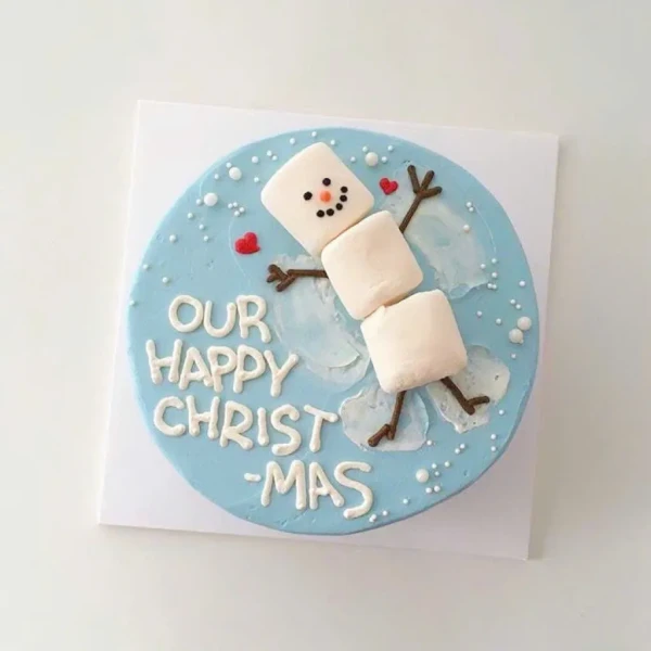 Blue cake with a marshmallow snowman angel, "Our Happy Xmas" text, and white dots.