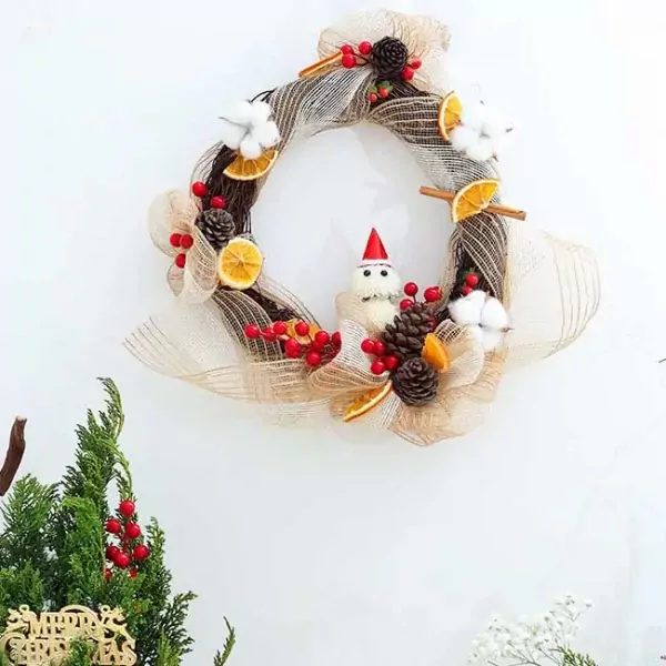 Christmas wreath with snowman, pinecones, dried oranges, berries, and cotton balls on white background.