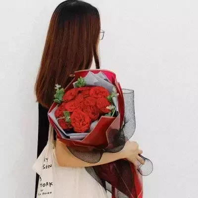 Woman holding a bouquet of red roses with light-colored wrapping.