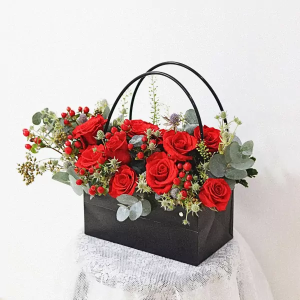 A black flower basket filled with vibrant red roses, berries, and greenery.
