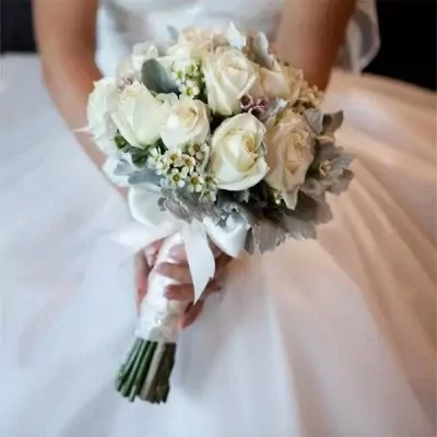 White roses and greenery bouquet in a bride's hands.
