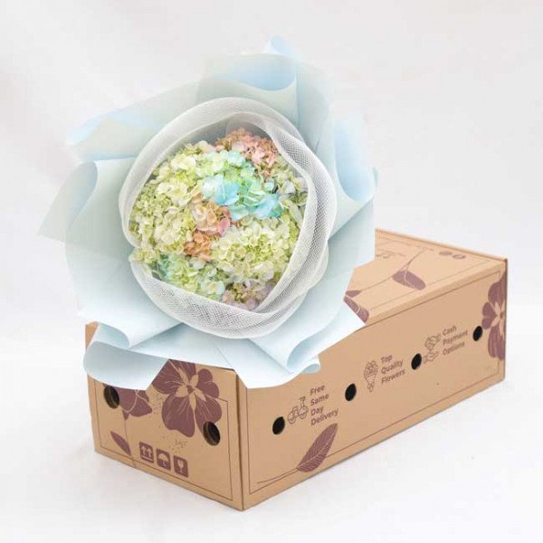 Pastel hydrangea bouquet in light blue wrapping sits atop a floral-decorated delivery box.