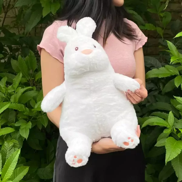 White plush bunny with pink nose and paw pads held by a person in a pink shirt.