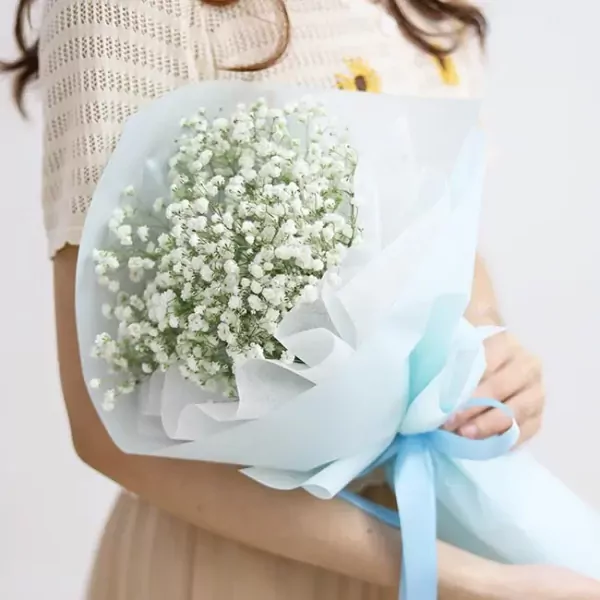 A woman holds a delicate bouquet of white baby's breath wrapped in light blue paper and tied with a blue ribbon.