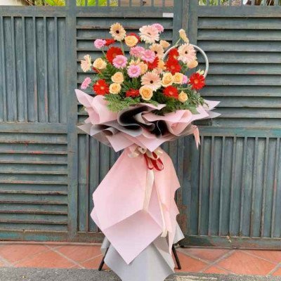 A large, colorful floral arrangement featuring gerbera daisies in pink, red, and yellow, presented on a stand.