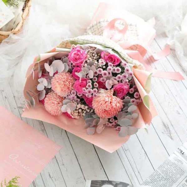 Bouquet of pink roses, peonies, and chrysanthemums with eucalyptus in pink paper.