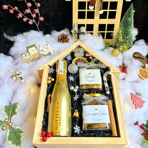 Christmas gift box with champagne, cookies, granola, and festive decorations.