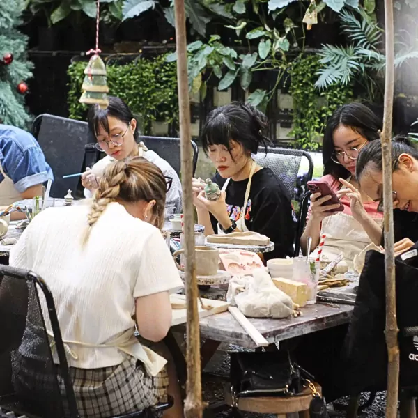 People in an outdoor pottery workshop creating air-dry clay pieces at a table.