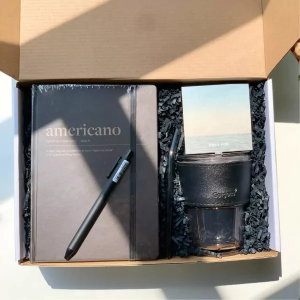 Gift box with "Americano" notebook, black pen, reusable cup, straw, and note card.