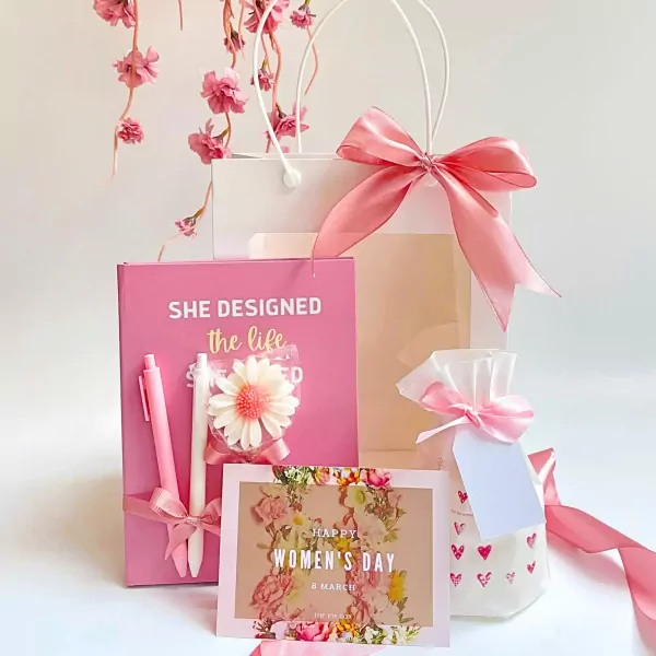 Pink gift set with notebook, pens, scented candle, and Women's Day card.