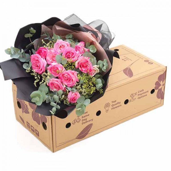 Pink roses and eucalyptus in black and brown wrapping, placed on a cardboard box.