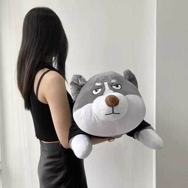 A woman holds a large, grumpy-faced husky plush toy.