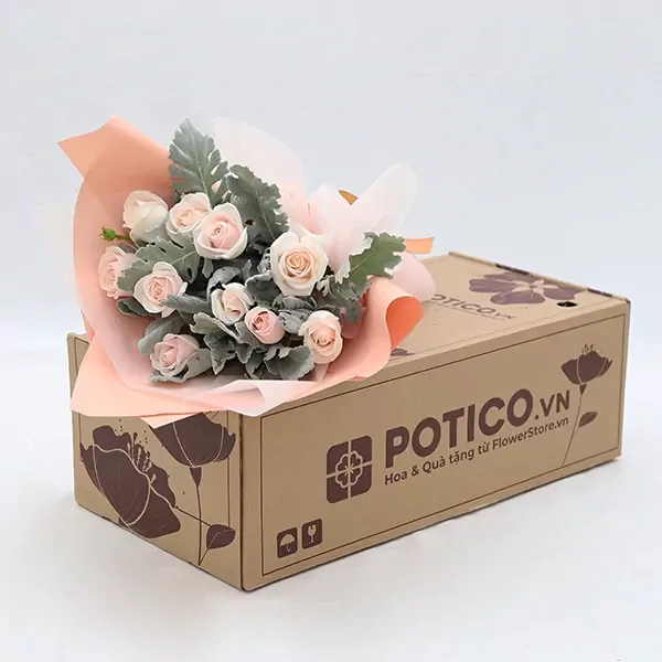 A bouquet of light pink roses and dusty miller on a brown gift box.