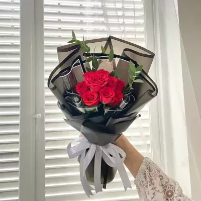 Red roses in black paper wrapping, tied with a white ribbon, held by a person's hand.