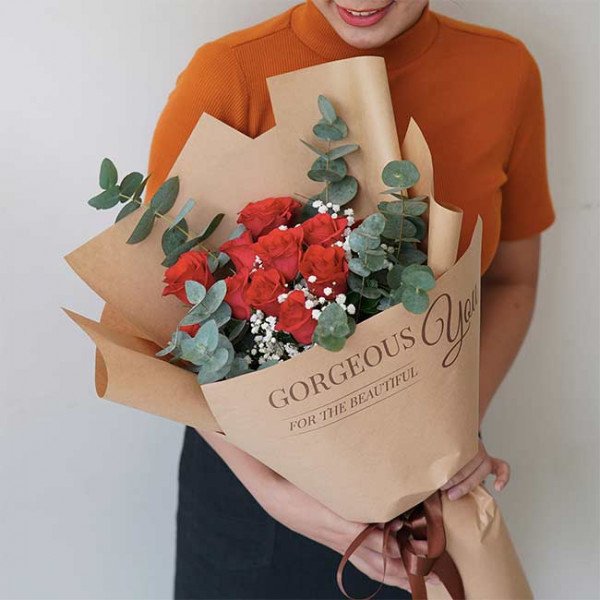Woman holding a bouquet of red roses wrapped in brown paper with "Gorgeous You" written on it.