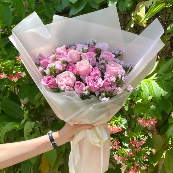 Pink and lavender roses in a bouquet wrapped in sheer paper, held by a hand with a black watch.