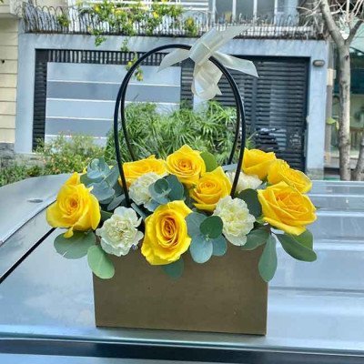 A box of yellow roses and white carnations with a ribbon bow.