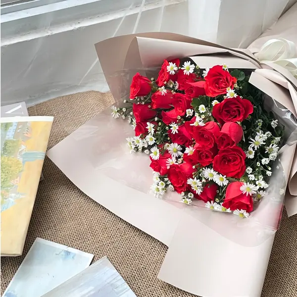Red roses and white daisies in a bouquet wrapped in cream paper.