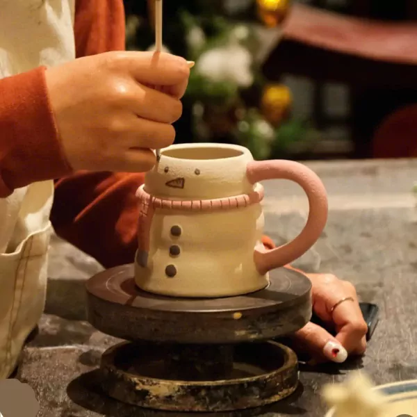 Person painting a snowman mug on a pottery wheel.