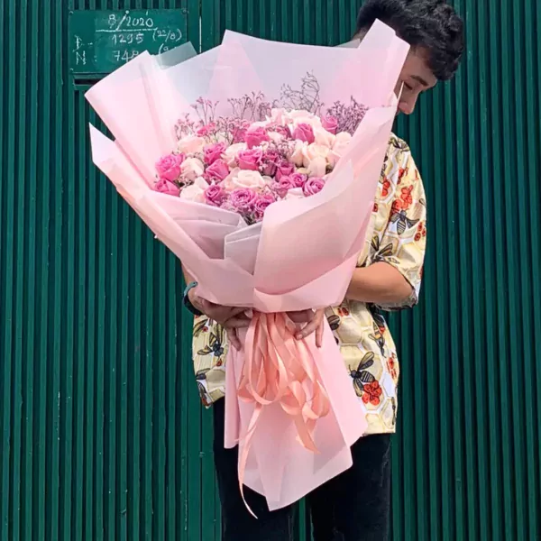 A man holding a large bouquet of pink and white roses wrapped in pale pink paper.