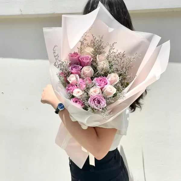 Woman holding a pastel bouquet of pink and white roses with delicate filler flowers.