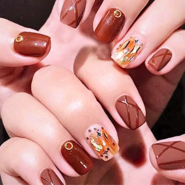 Close-up of a woman's hands with chocolate brown gel nails, some with a criss-cross design and others with gold accents.