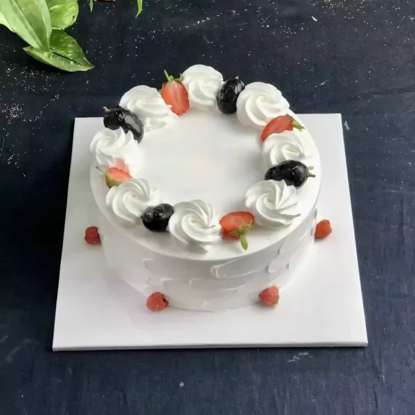 Round white cake with cream swirls, strawberries, blueberries, and raspberries.
