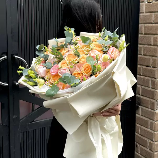 A woman in black holds a large bouquet of peach and pink roses, lisianthus, and chrysanthemum.