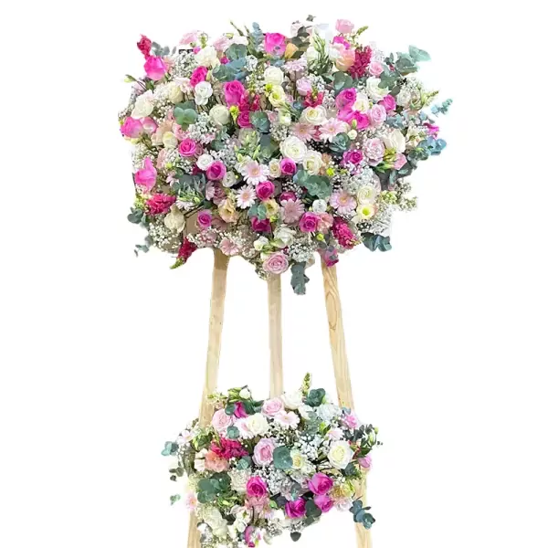 Two-tiered floral arrangement with pink, white, and cream roses, daisies, and other greenery on a wooden stand.