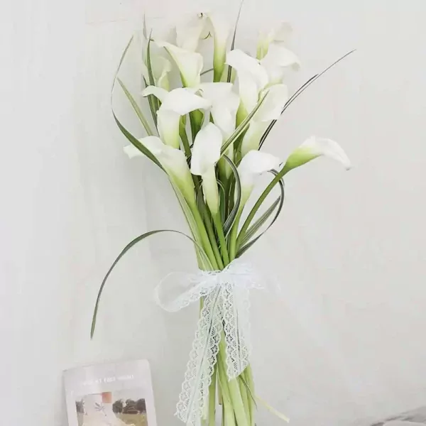 Bouquet of white calla lilies tied with white lace ribbon, with a book in the foreground.
