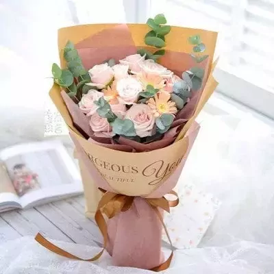 Pink roses and gerbera daisies bouquet with eucalyptus, wrapped in kraft paper with text.