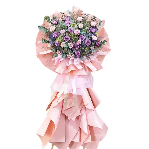 Large floral arrangement with purple and pink roses, hydrangeas, and greenery in pink wrapping.