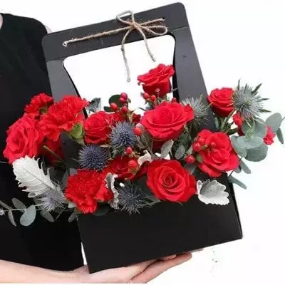 A black basket overflowing with red roses, carnations, and thistles.