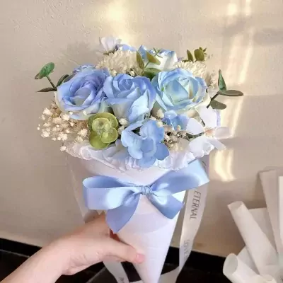 Blue roses and white flowers in a cone bouquet with a blue bow.