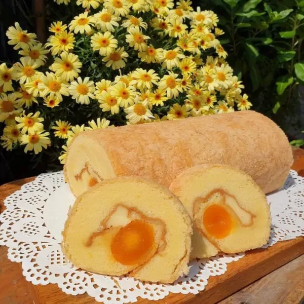 A six-piece egg floss roll with a creamy filling sits on a white doily beside yellow flowers.