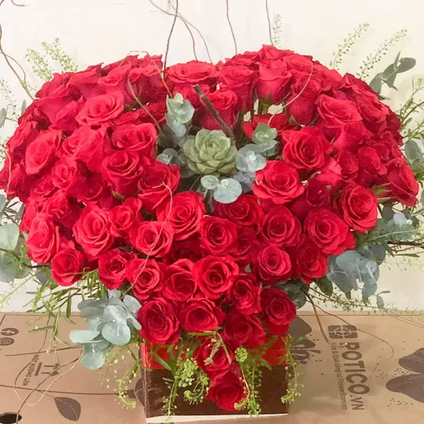 Heart-shaped bouquet of 99 red roses, succulent, and eucalyptus in a box.